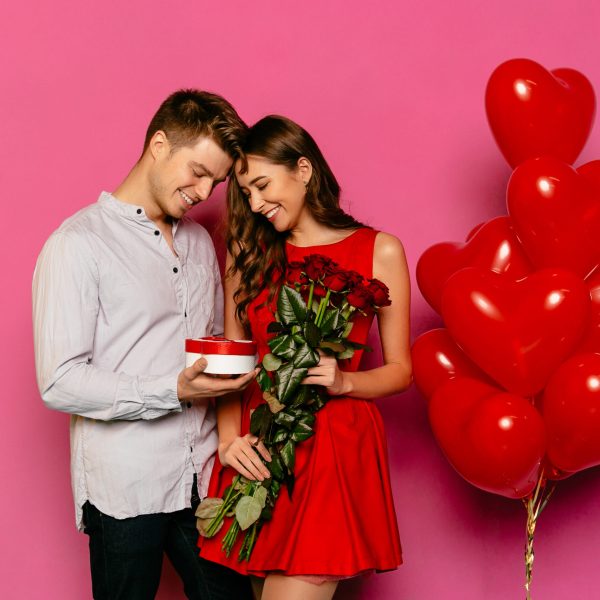 Handsome man and attractive woman looking at box with gift, red roses, balloons while celebrating a St. Valentine's day.